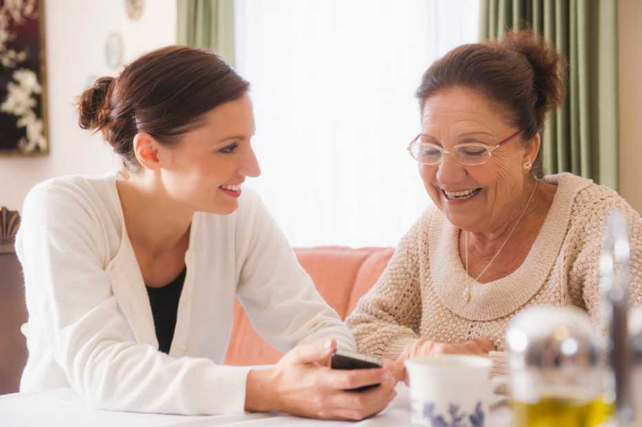 Young Caucasion female caregiver sitting with family member looking at a smartphone