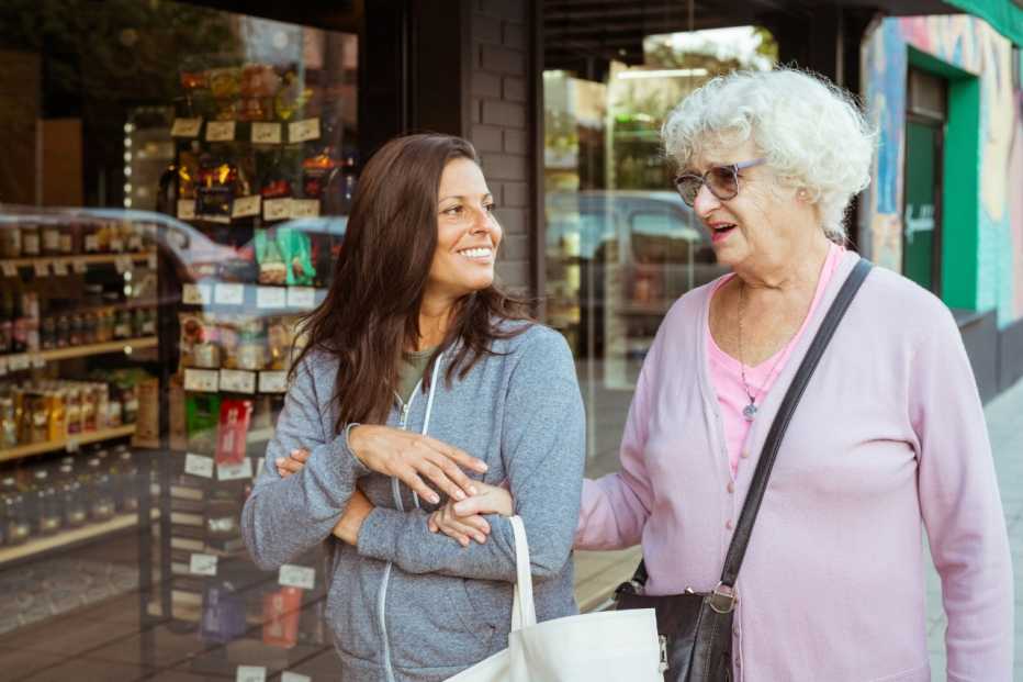 Smiling senior woman going to shopping with female, walking footpath arm in arm in the town.