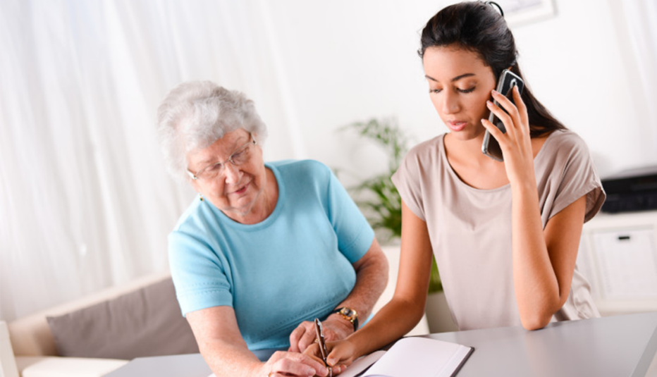 a caregiver on the phone trying to access her mother's medicare information a woman on the phone taking notes with her mother next to her