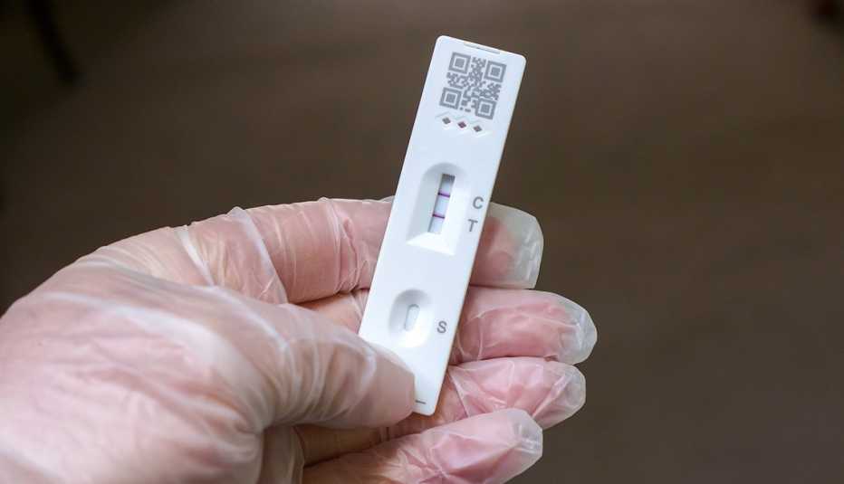 Gloved hand holding a COVID test result strip.