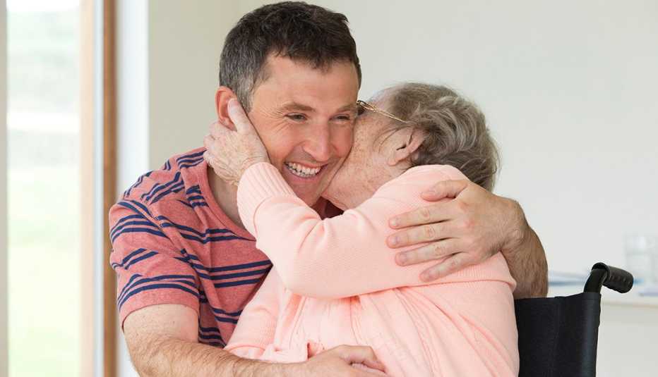 A woman in a wheelchair giving her adult son a kiss on the cheek as he hugs her