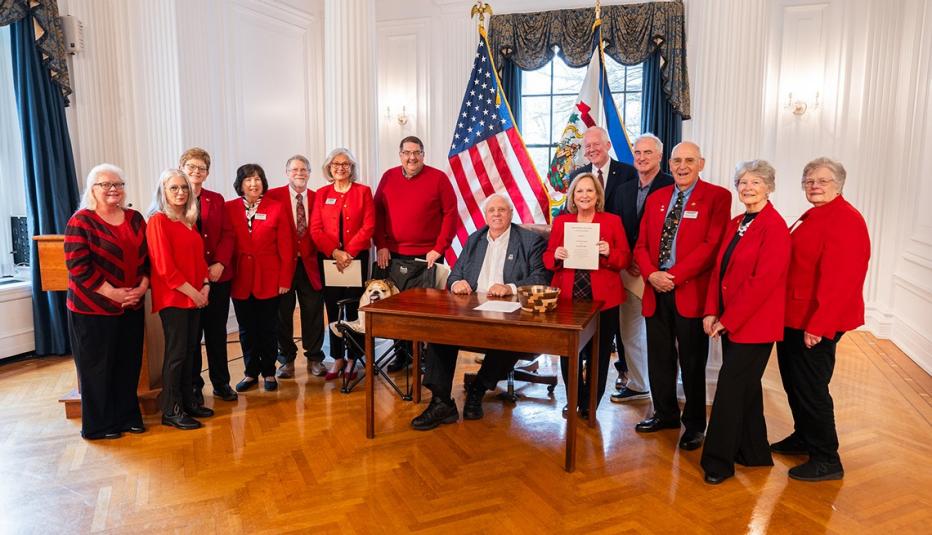 AARP West Virginia Helps Pass Law to End Tax on Social Security group of people in red shirts are around a man sitting at a table