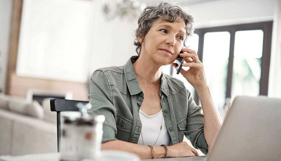 Shot of a mature woman making a phone call while working on her laptop at home