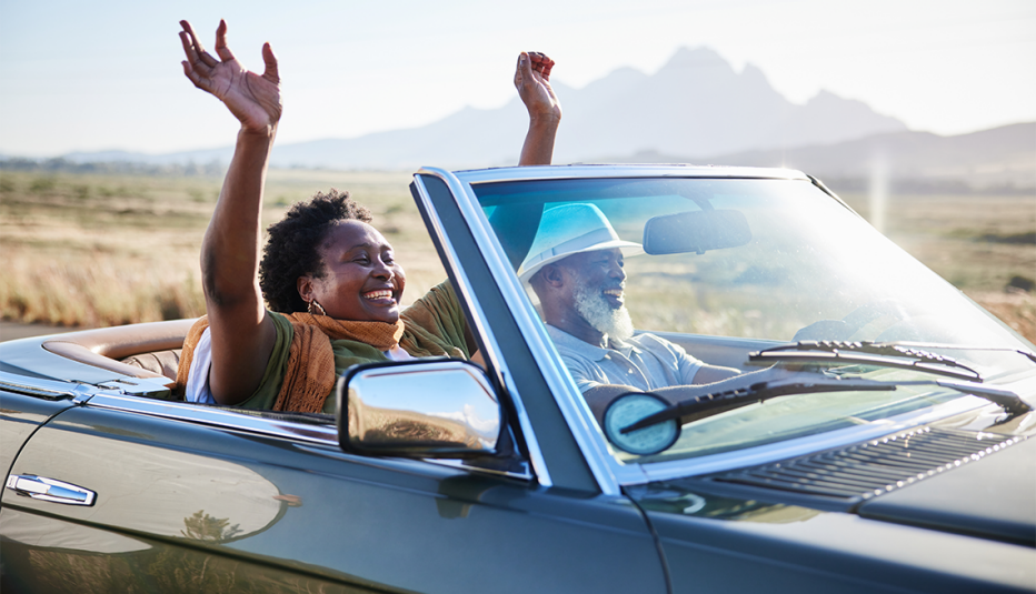 a woman puts her hands up as a man drives her in a convertible on a summer road trip a woman puts her hands up as a man drives her in a convertible on a summer road trip
