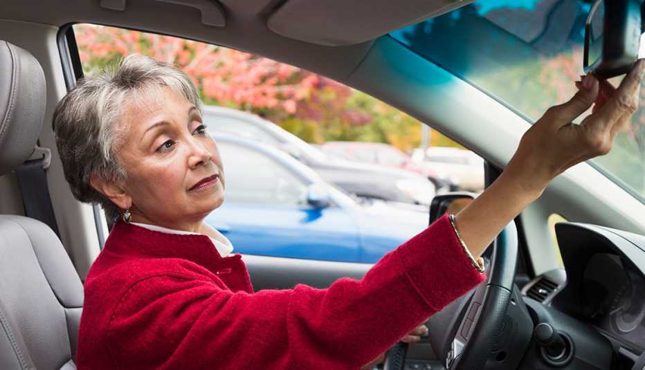 a woman in a red jacket adjusts her car mirror