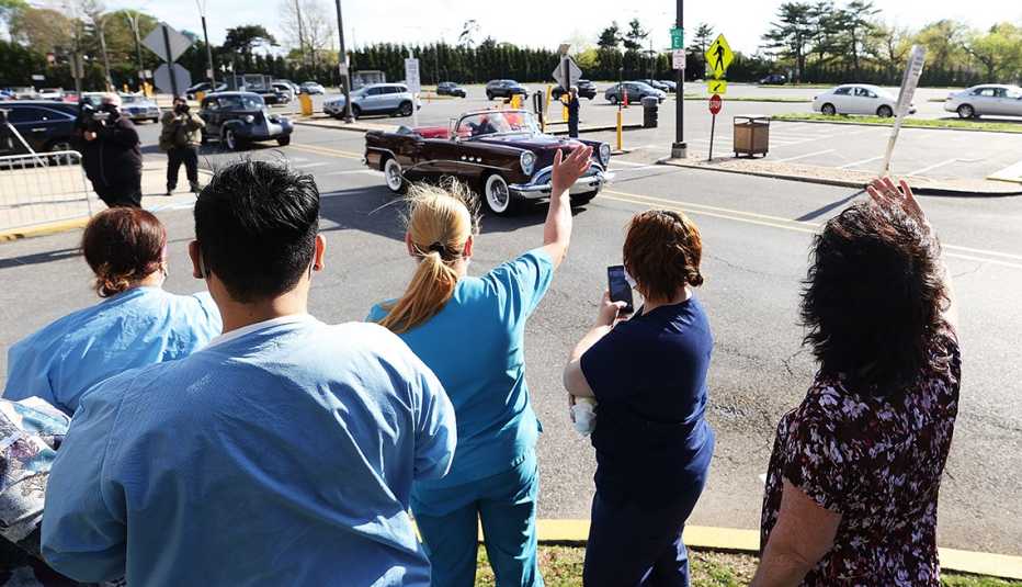 healthcare workers outside of a hospital wave to a passing parade of class cars organized in their honor during the coronavirus pandemic