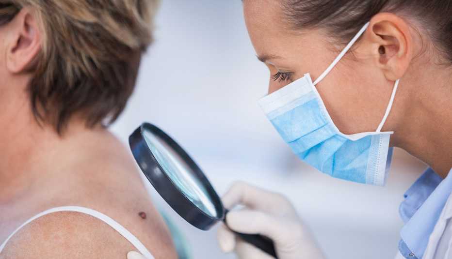 Dermatologist using a magnifying glass to examine female patient&rsquo;s mole