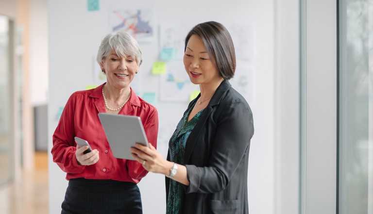 Two women in a work environment standing and looking at something on a tablet together