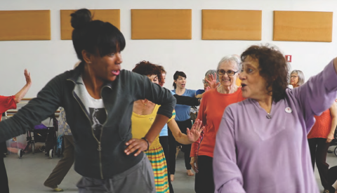 Two women dancing in a room in front of other women