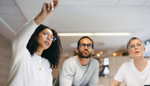 A woman pointing offscreen in a work meeting with a man and another woman