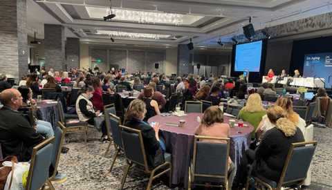A conference room filled with people sitting at round tables