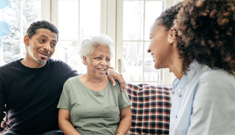 A man and older woman sitting on a couch at home and talking to a female healthcare professional