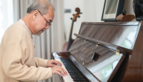 A man playing a piano with another string instrument in the background