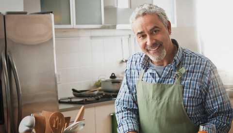 A man smiling and wearing a chef apron in a home kitchen