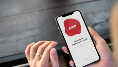 A woman's hands holding a smartphone with the AARP Staying Sharp app on the screen
