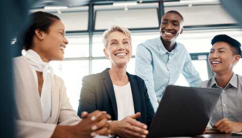Four smiling people working together on a laptop in an office setting