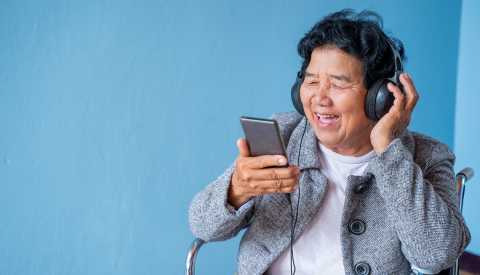 A woman in a wheelchair wearing headphones and listening to music from a phone