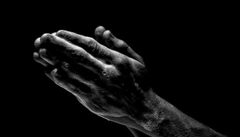 A close-up view of a set of hands touching in prayer with a black background