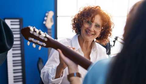 Two women in a guitar class together with one of them teaching the other