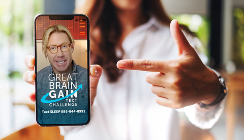 A woman pointing at a held out phone showing the image of a man and the text "Great Brain Gain Text Challenge"