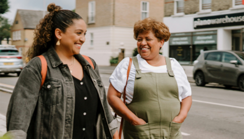 Two smiling women walking on a sidewalk in a town together