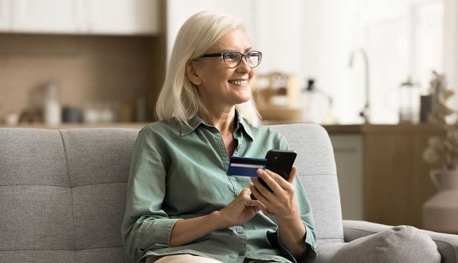 A smiling woman holding a credit card and phone, shopping online