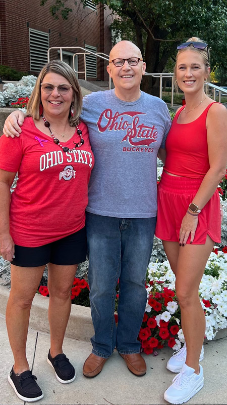 Steven standing outdoors with his wife and daughter, all wearing Ohio State colors