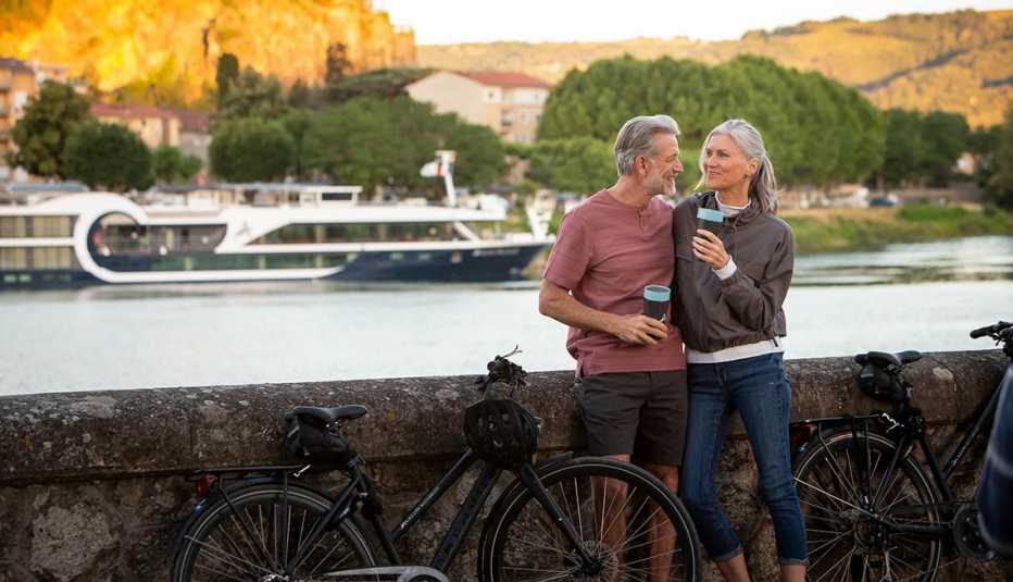 A couple is standing by a flowing river, with two bikes nearby. A couple is standing by a flowing river, with two bikes nearby.