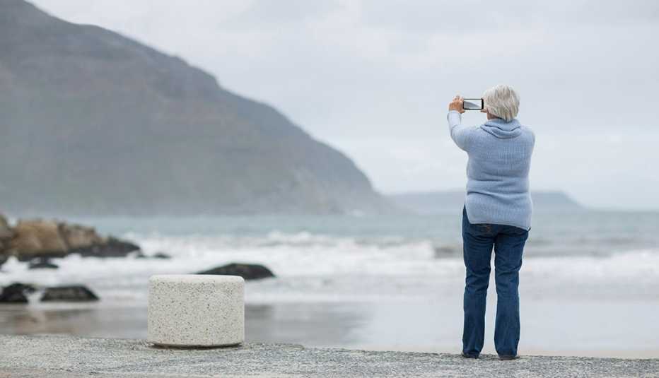 A woman capturing beautiful mountain view standing on the paved surface of sea beach