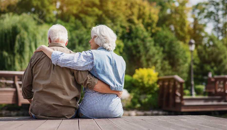 An outdoor medium-shot image of a couple sitting side-by-side with their backs mostly to the viewer.