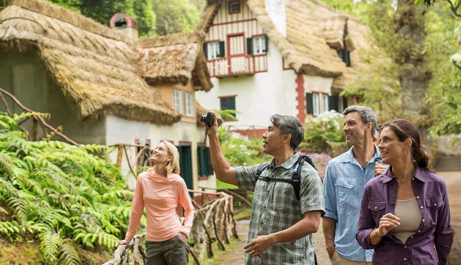 Several individuals gather to take a picture in front of a charming thatched-roof house amidst a natural setting