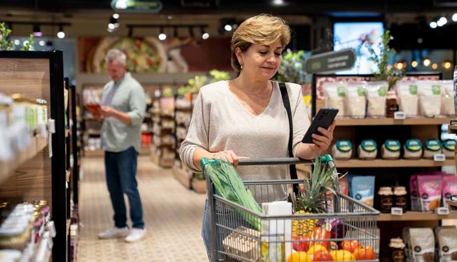 A woman buying groceries at the supermarket following a shopping list on her cell phone