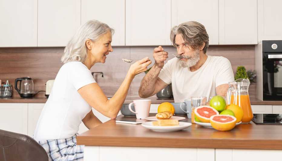 A man and woman at their kitchen counter eating with spoons