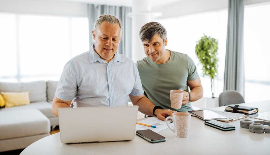 A wide shot shows two adult men looking at a laptop in a well-lit room