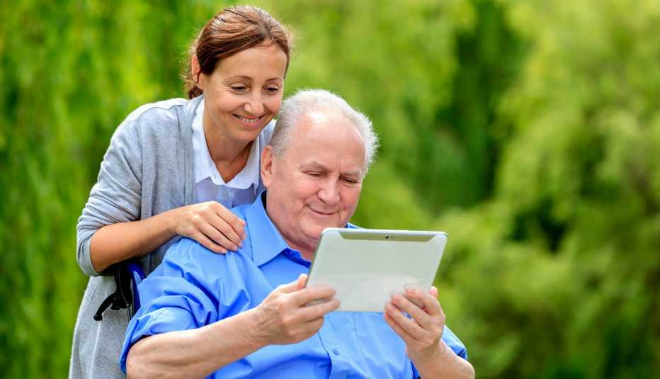 caregiver looks over shoulder of man holding a tablet 