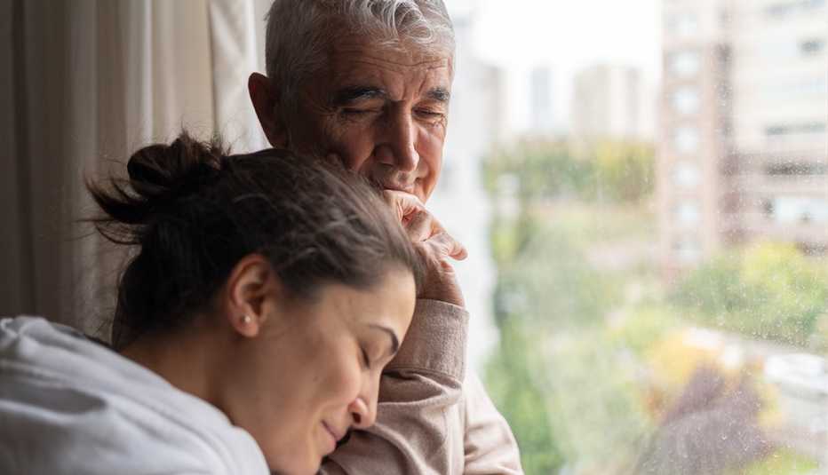 Daughter embraces her father as they stand in front of a window.