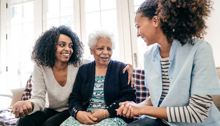 A woman sits on the couch with her elderly mother and a friend