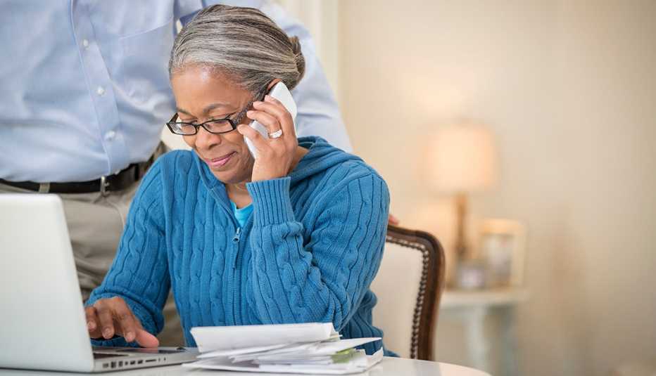 A woman on a call on a cell phone while sitting and using a laptop