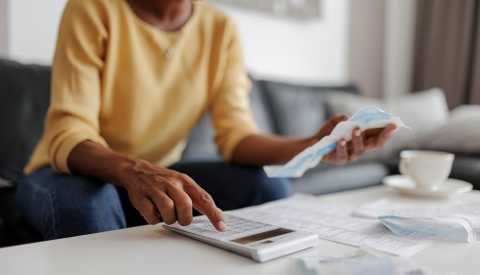 close up of an adult woman using a calculator to add up bills at home, sitting in her living room