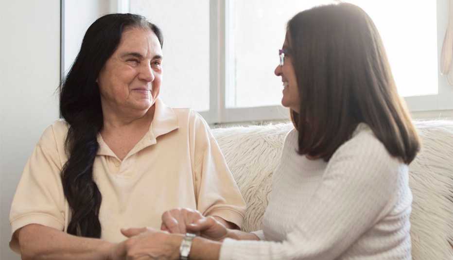 Smiling older woman and her daughter are sitting, looking at each other and holding hands