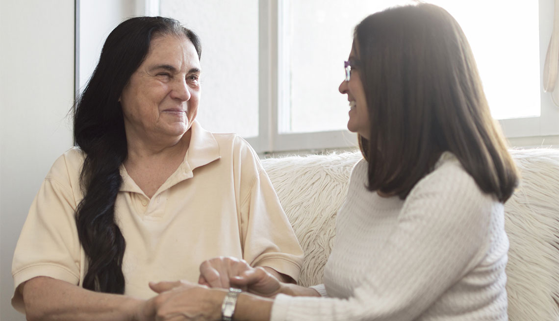 Smiling older woman and her daughter are sitting, looking at each other and holding hands