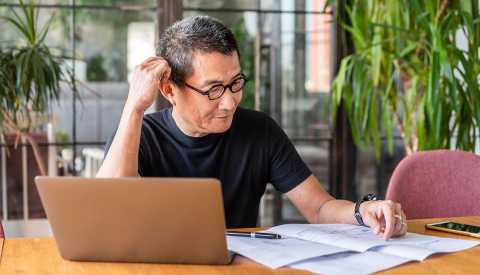 Man looking at a computer and paperwork as he plans his own funeral Man looking at a computer and paperwork as he plans his own funeral