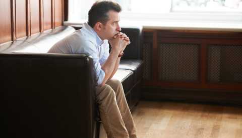 A man sitting on a sofa, looking sadly into the distance  A man sitting on a sofa, looking sadly into the distance