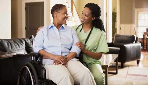 Woman in wheelchair talking with a female nurse inside a home