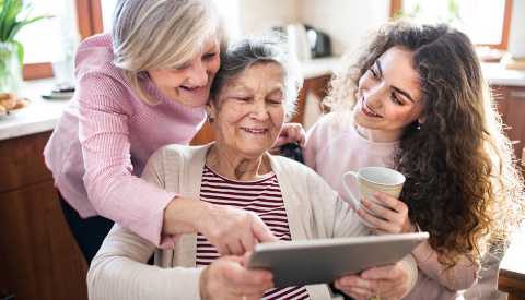A woman with her mother, who is in a wheelchair and her teenage daughter. All are looking at a tablet together A woman with her mother, who is in a wheelchair and her teenage daughter. All are looking at a tablet together