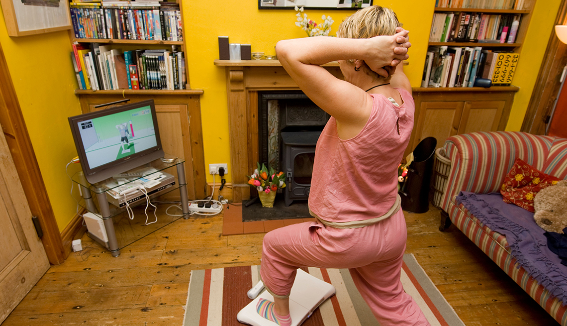 How Caregivers Can Find the Time to Exercise, Mature woman doing yoga exercises on a Nintendo Wii Fit in the living room of her house, How Caregivers Can Find Time to Exercise