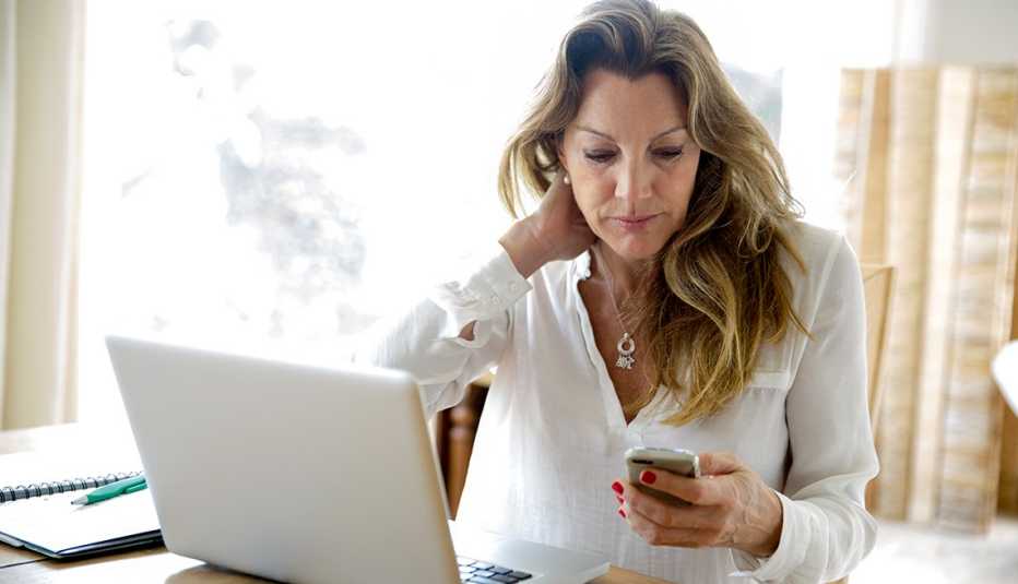 Woman at work with a laptop in front of her, being distracted by a message from home on her mobile phone