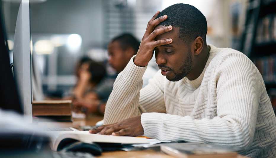 A male college student studying in a library and looking stressed