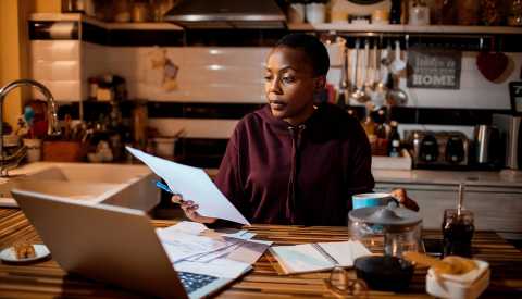 a woman sitting at a laptop and looking through bills looking stressed a woman sitting at a laptop and looking through bills looking stressed
