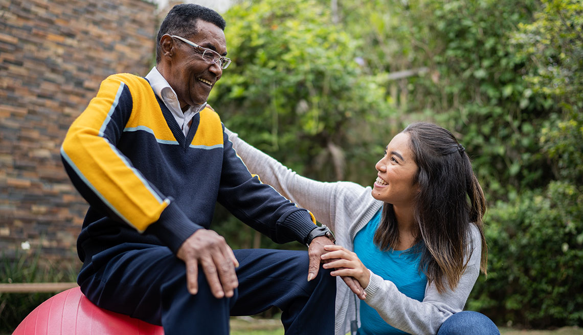 caregiver helping man sitting on an exercise ball